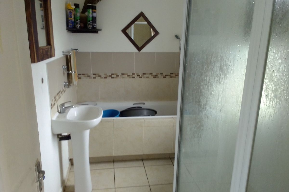 A functional bathroom featuring a pedestal basin, a tiled bathtub, and a separate glass-enclosed shower unit with neutral wall and floor tiling.