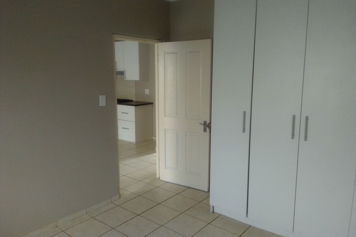 A bedroom featuring built-in cupboards and tiled flooring, with a view through the doorway into an adjacent kitchen area.