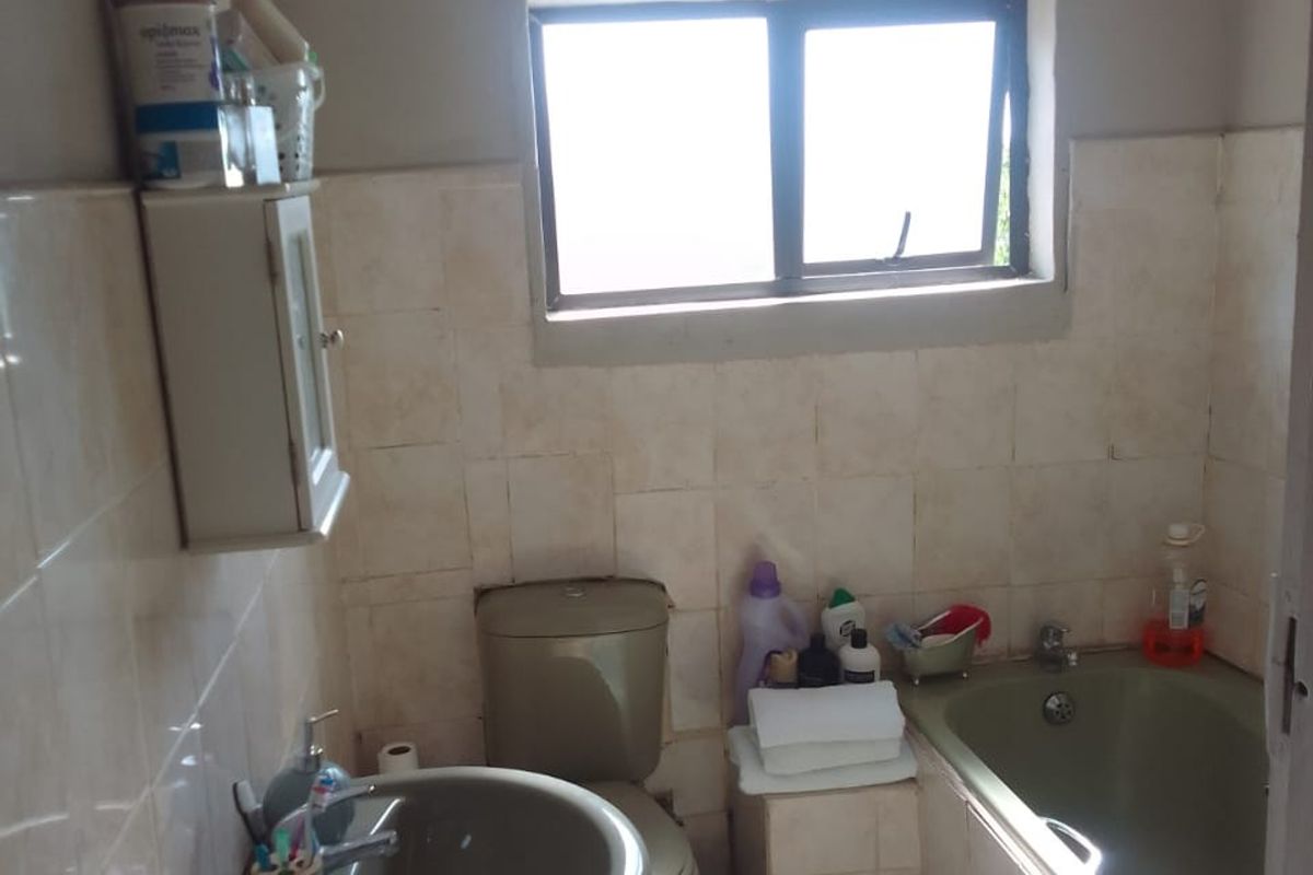 A functional bathroom featuring a pedestal basin, toilet, and a built-in bathtub with tiled splashbacks and a window for natural light.