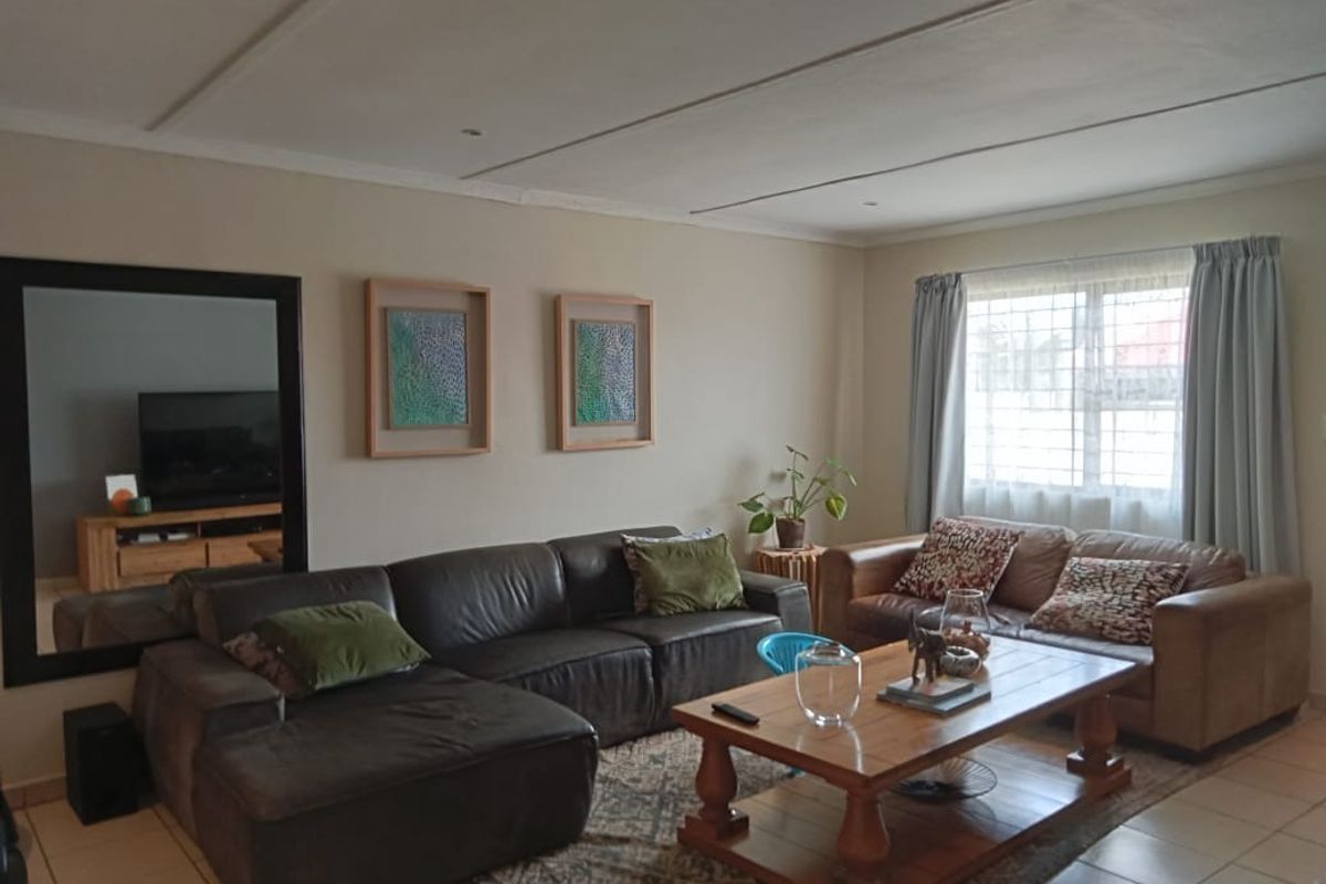 A comfortable living room featuring tiled flooring, large window with security bars, and neutral wall finishes.