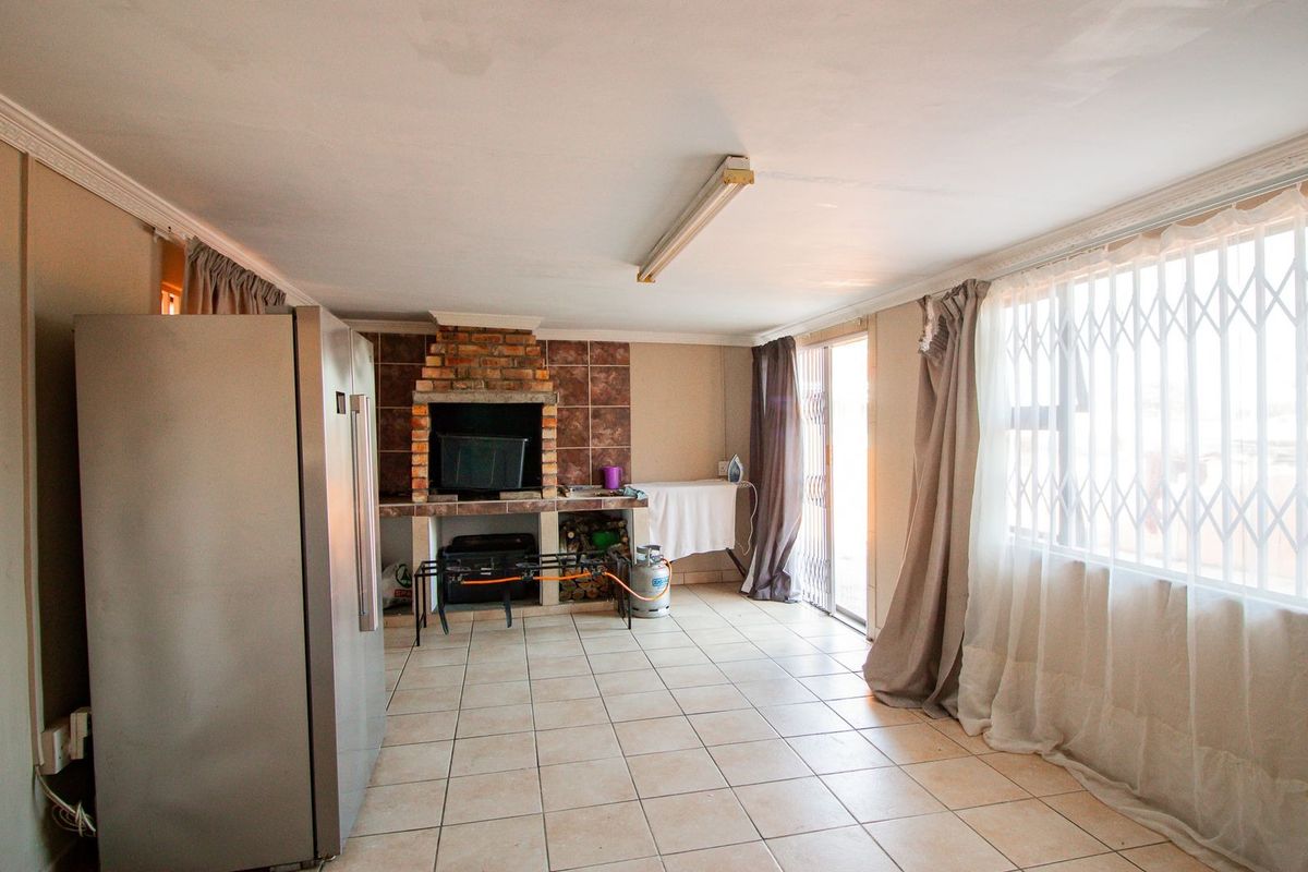Spacious living area featuring a built-in brick fireplace, tiled flooring, and large windows with security gates, offering a functional space for relaxation.