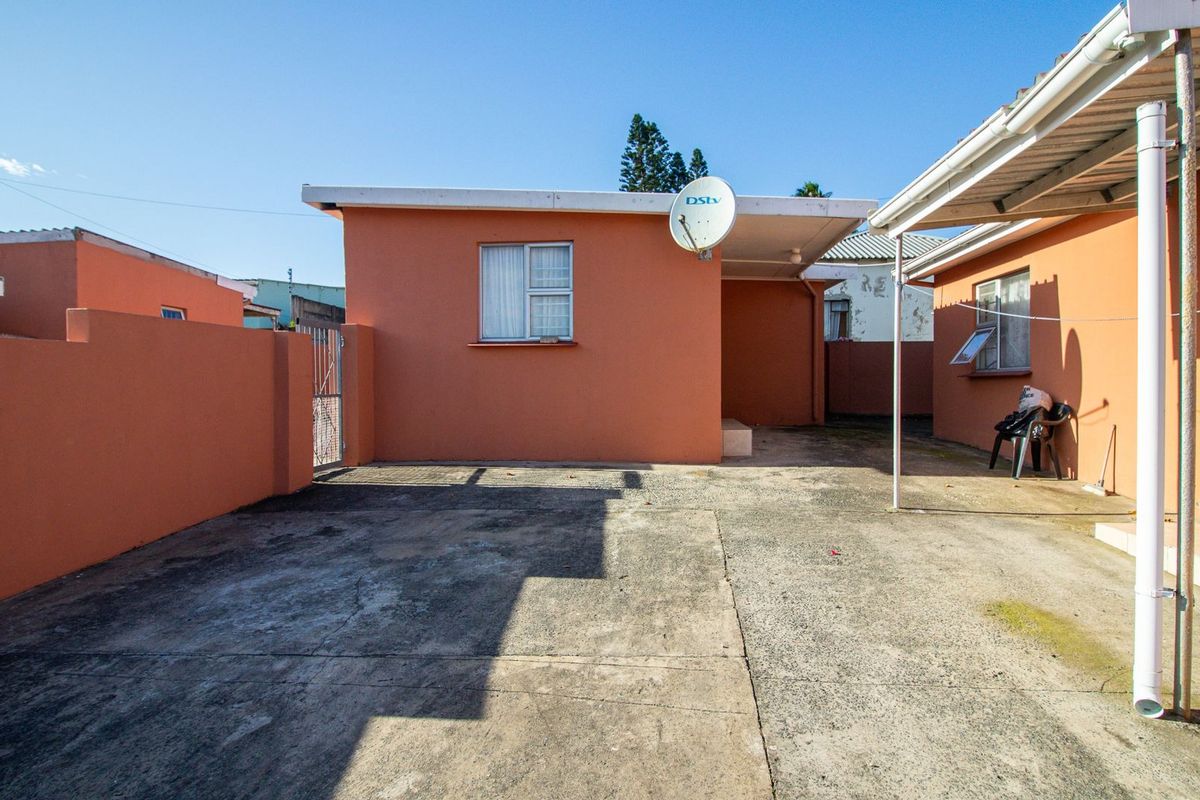 A rear exterior view of the property featuring a paved courtyard area, perimeter boundary walls, and a covered patio section.