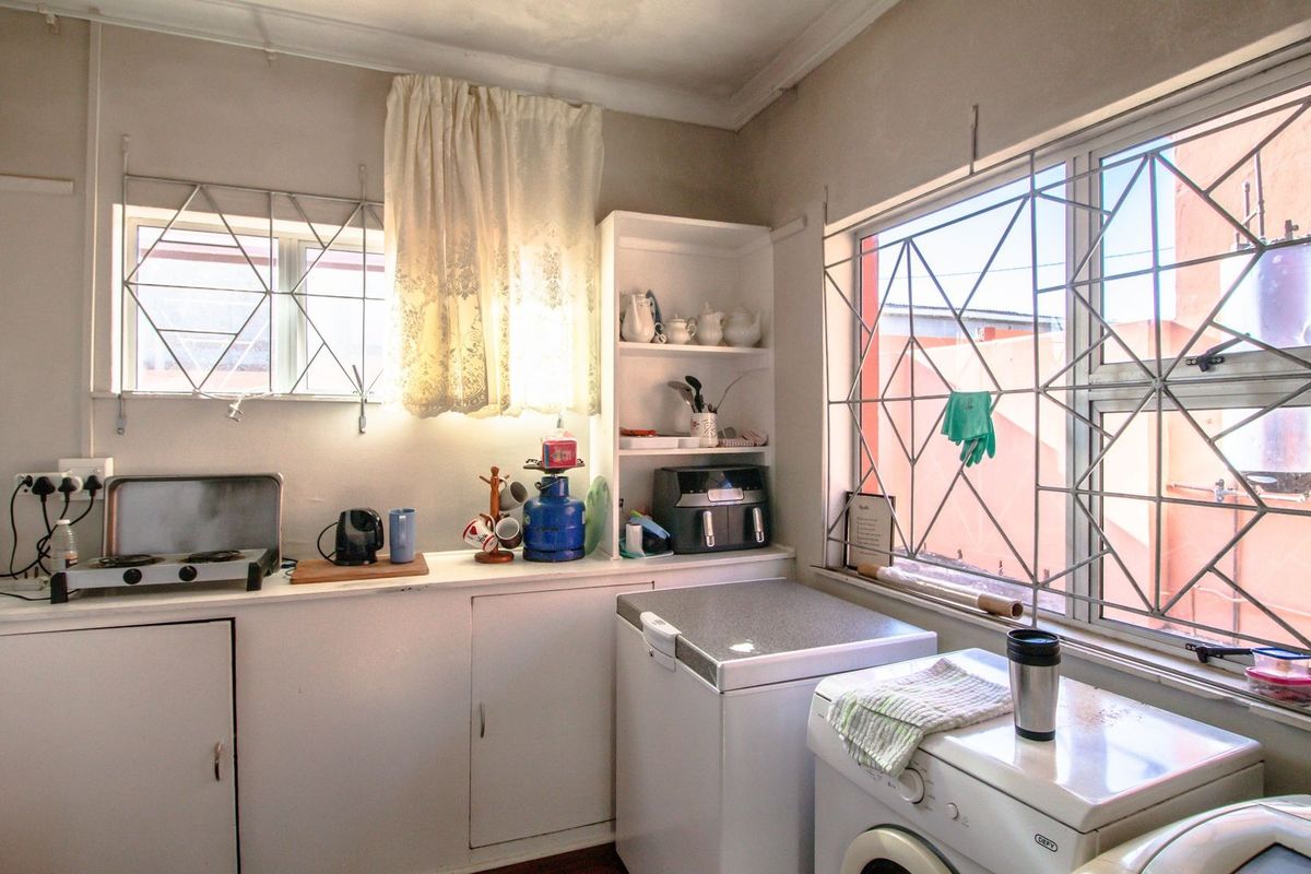 A functional kitchen area featuring built-in cabinetry, shelving, and dedicated space for laundry appliances, with security bars installed on the windows.