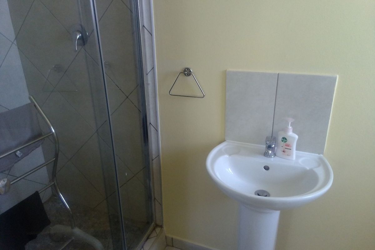 A functional bathroom featuring a pedestal basin with tiled splashback and a glass-enclosed shower unit.