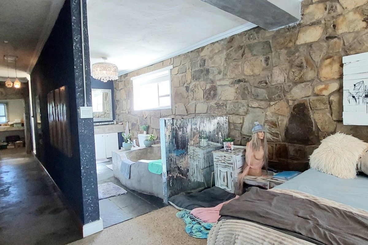 A unique bedroom featuring exposed natural stone walls, an integrated open-plan bathroom area with a built-in bathtub, and a long connecting hallway.