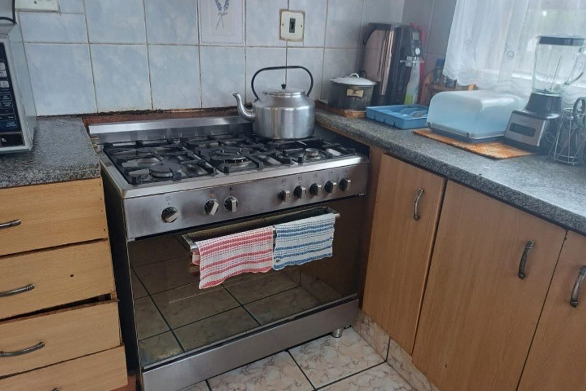 A functional kitchen area featuring a stainless steel gas stove, granite-look countertops, and tiled splashbacks with wooden cabinetry.