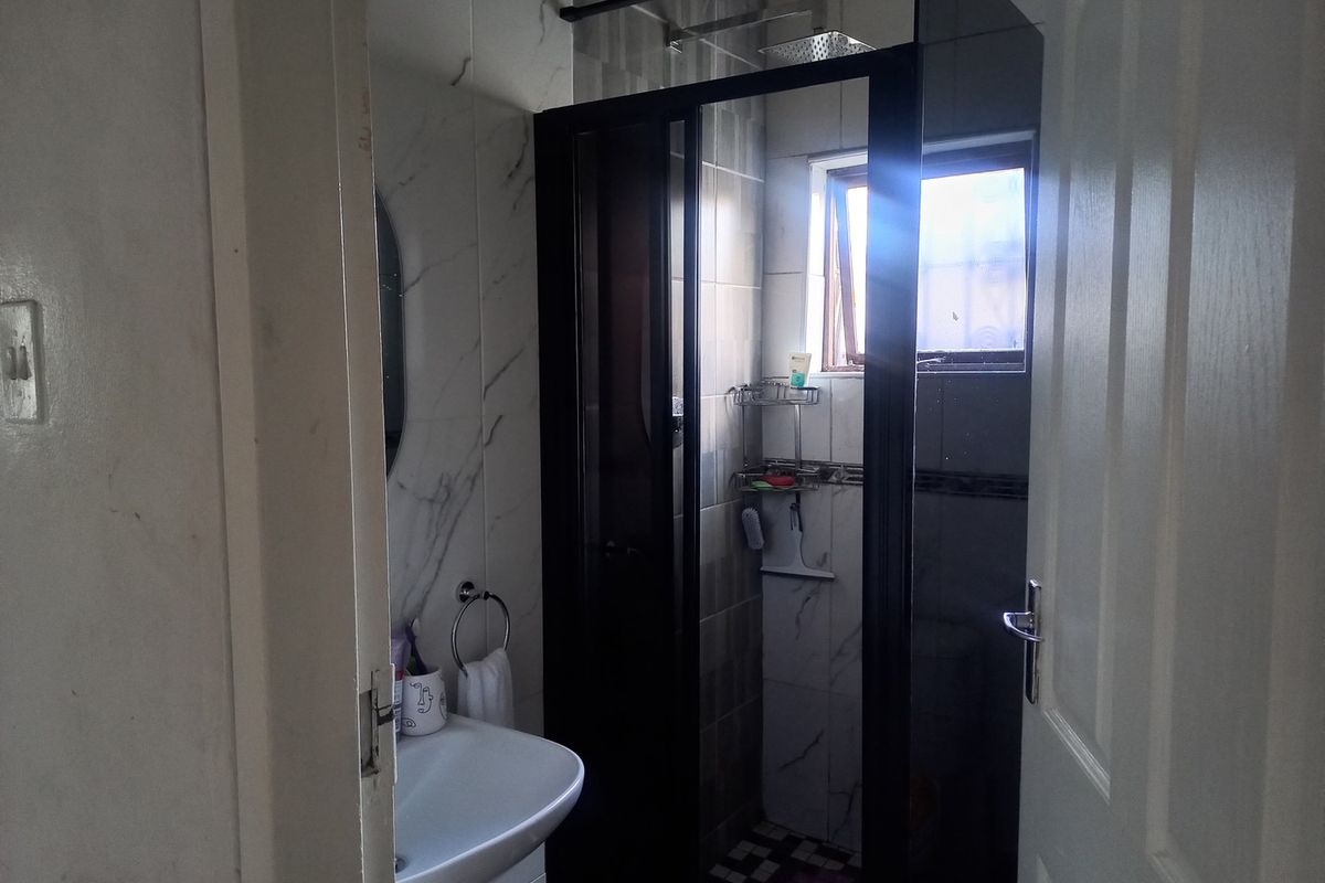 A compact bathroom featuring a modern glass-enclosed shower, wall-mounted basin, and marble-effect wall tiling.