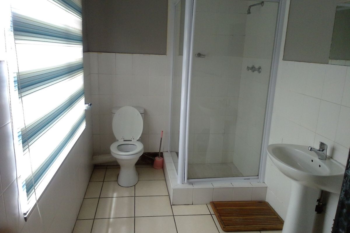 A functional bathroom featuring a pedestal sink, a glass-enclosed shower stall, and a standard toilet with tiled flooring and walls.