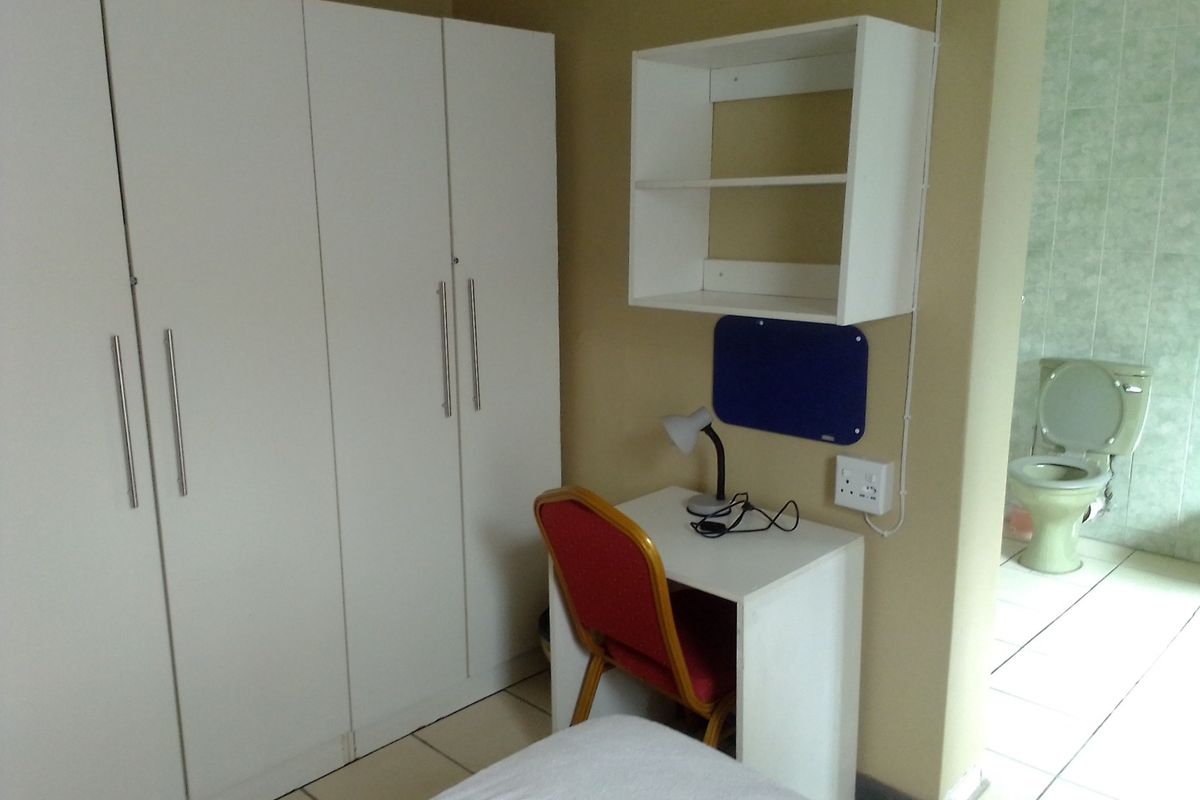 A bedroom featuring built-in white cabinetry, a study nook with shelving, and an adjoining bathroom with tiled finishes.