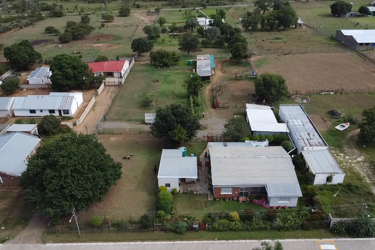 Aerial view of a small holding property featuring multiple outbuildings, fenced paddocks, and established garden areas on a spacious rural plot.