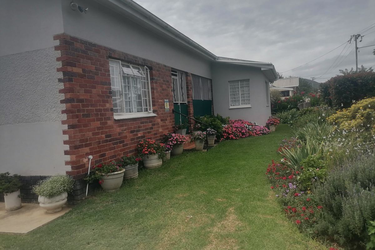 A view of the side exterior of the small holding, featuring a brick and plaster facade, security gates, and a well-maintained garden.