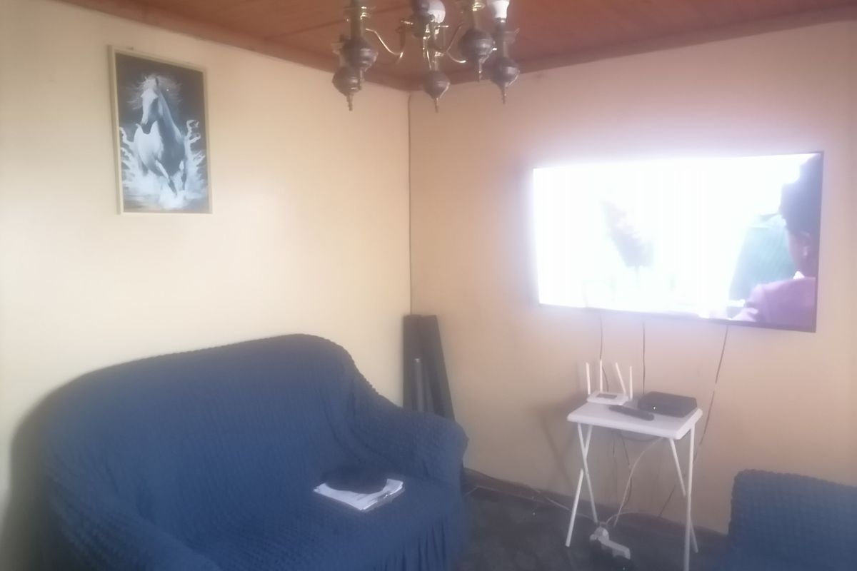A living room featuring a timber-clad ceiling, wall-mounted television, and tiled flooring.