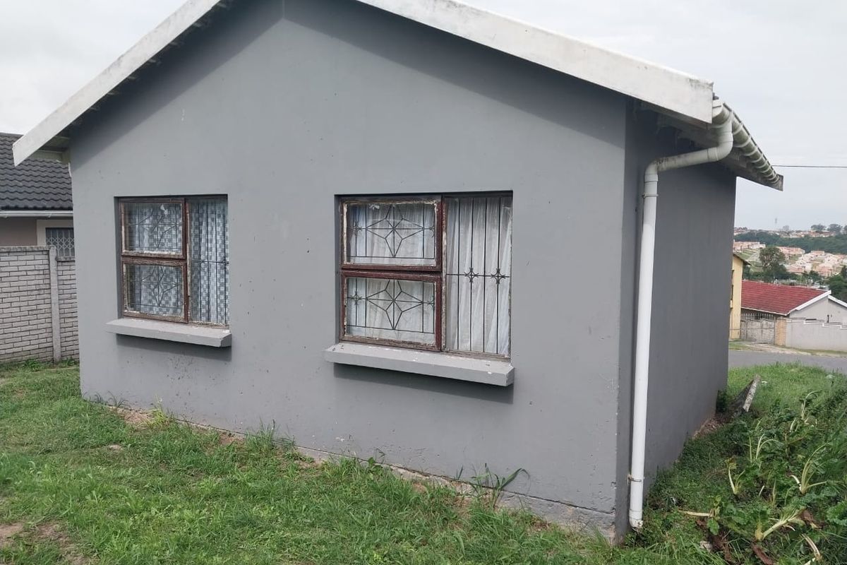 A side view of a residential house featuring grey painted exterior walls, metal window frames with security bars, and a functional rainwater downpipe system.