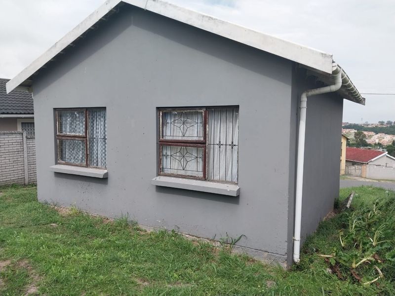 A side view of a residential house featuring grey painted exterior walls, metal window frames with security bars, and a functional rainwater downpipe system.