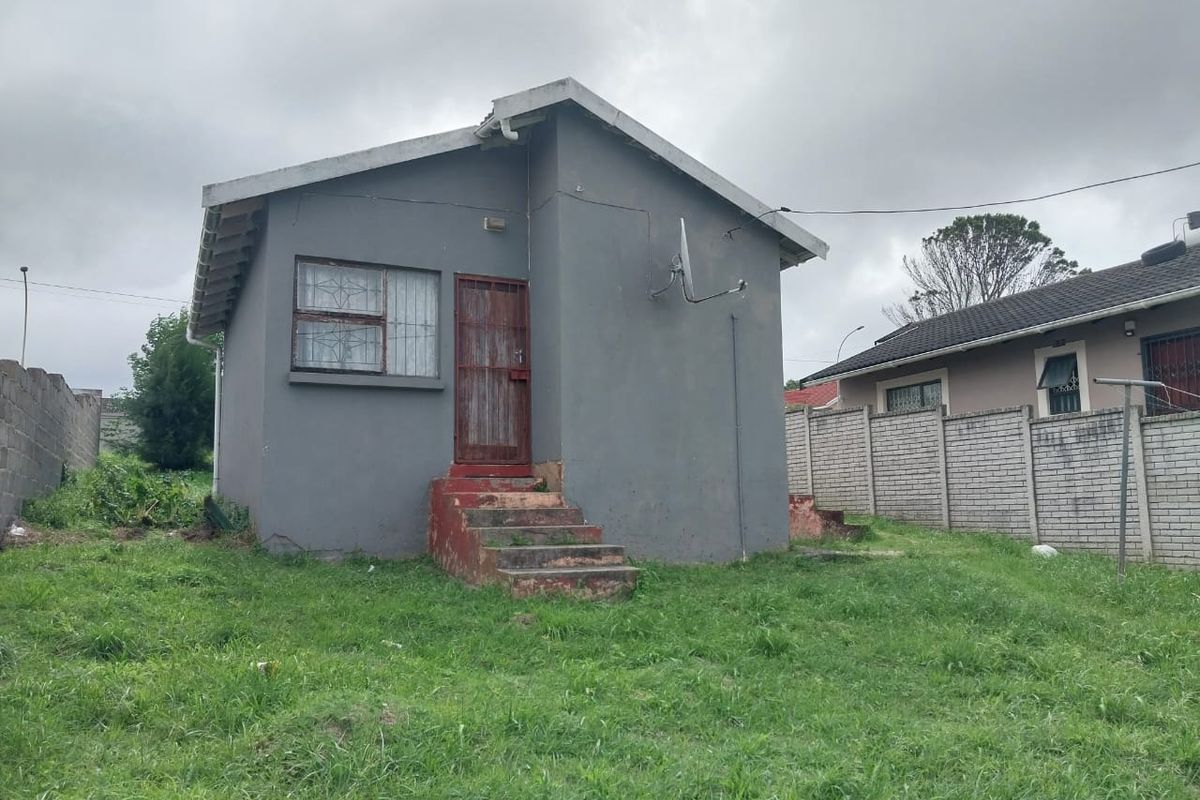 Rear view of a detached house featuring a grey painted facade, concrete entrance steps, and perimeter boundary walling.