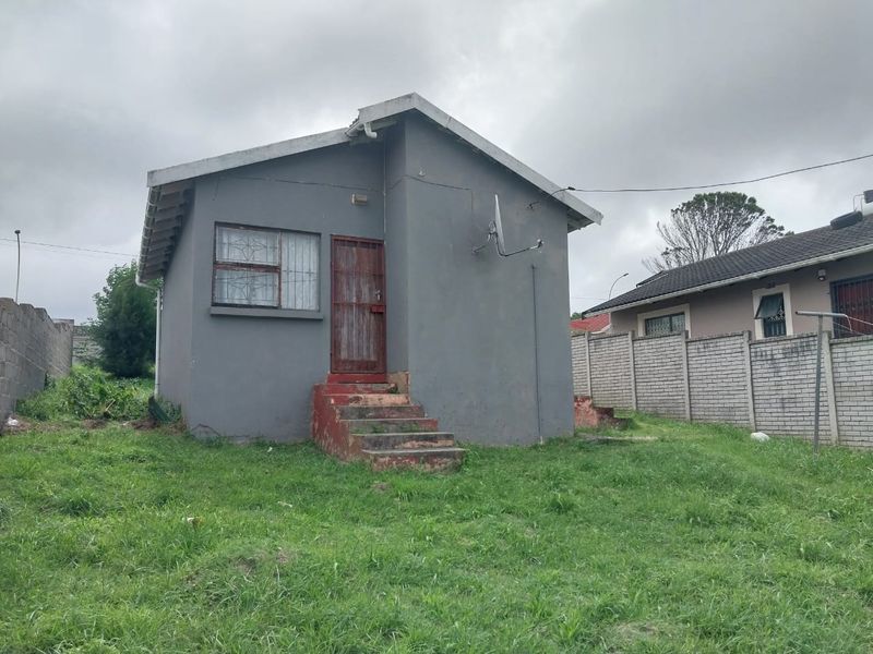 Rear view of a detached house featuring a grey painted facade, concrete entrance steps, and perimeter boundary walling.