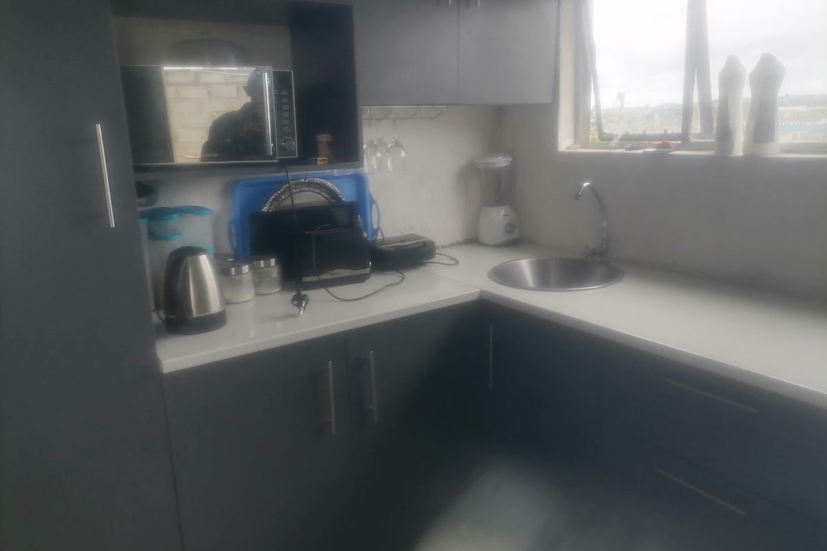 Compact kitchen area featuring dark grey cabinetry, white countertops, a stainless steel sink, and a built-in microwave space.