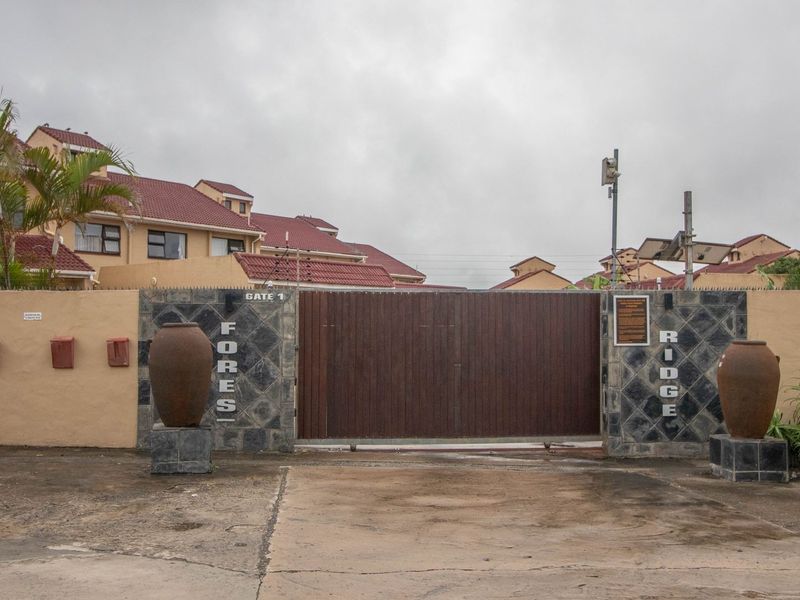The main entrance gate to Forest Ridge townhouse complex, featuring a secure automated gate, perimeter wall with electric fencing, and paved driveway access.