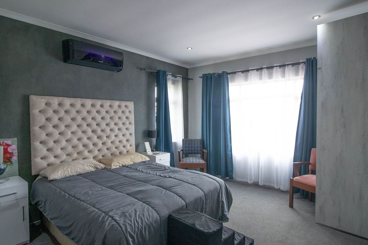 A well-maintained bedroom featuring neutral carpet flooring, recessed downlighting, a wall-mounted air conditioning unit, and integrated built-in wardrobe storage.