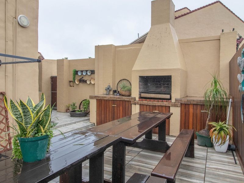 Outdoor patio area featuring a built-in braai, tiled flooring, and enclosed by boundary walls and wooden fencing, ideal for outdoor entertaining.