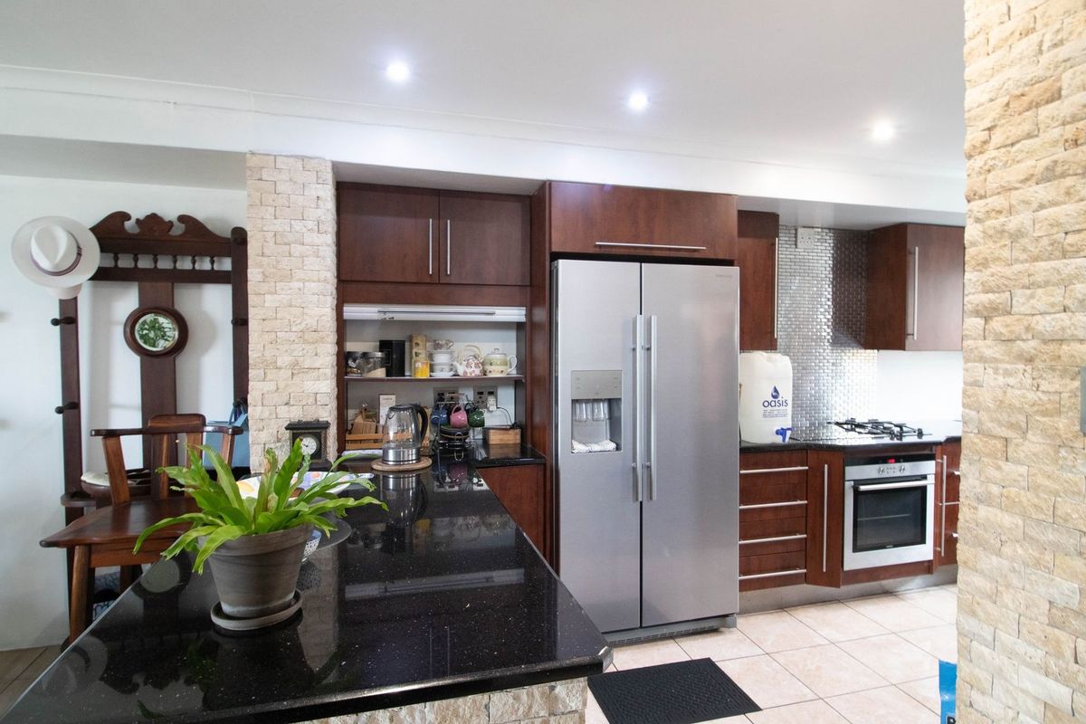 Modern kitchen featuring dark wood cabinetry, granite countertops, stone cladding accents, and integrated stainless steel appliances, offering a functional and stylish cooking space.