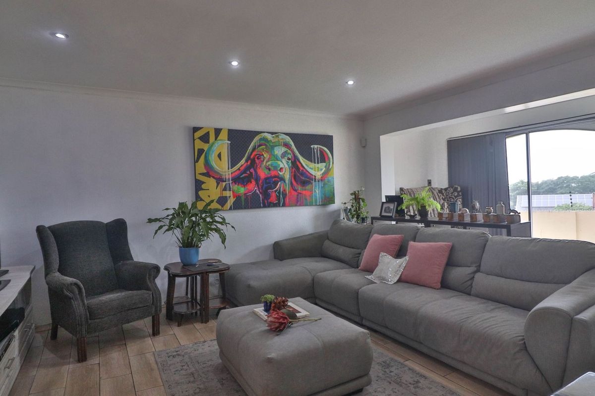 A well-lit living room featuring tiled flooring, recessed downlights, and a large sliding glass door providing access to the exterior.