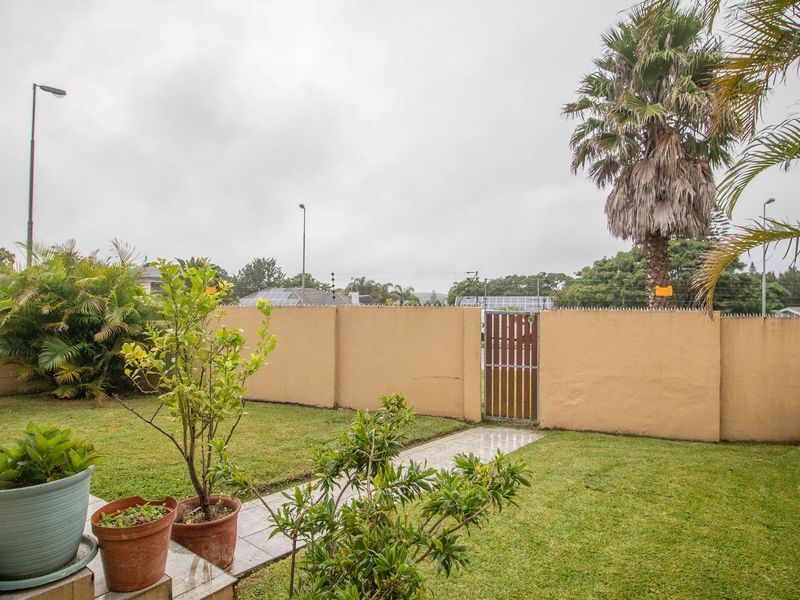 A private rear garden featuring a lawn, tiled patio area, and secure perimeter wall with a wooden pedestrian gate.