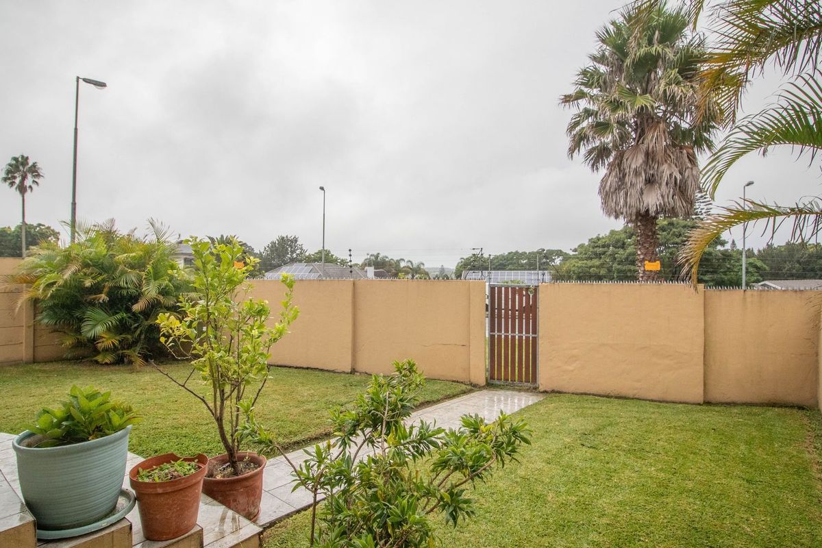 A private rear garden featuring a lawn, tiled patio area, and secure perimeter wall with a wooden pedestrian gate.