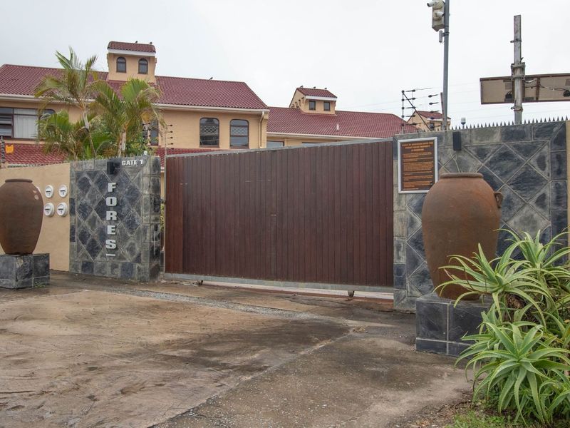 Front entrance of the townhouse complex featuring a large sliding security gate, stone-clad pillars, and integrated security infrastructure.