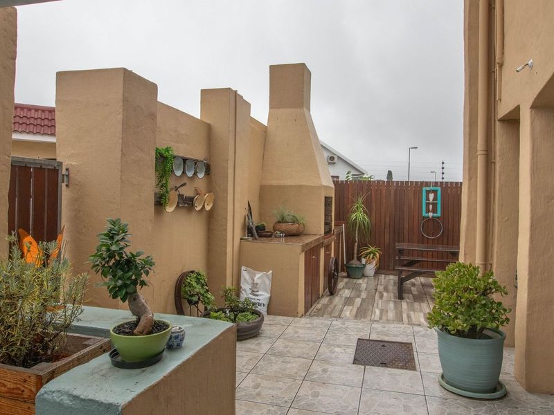 Outdoor patio area featuring a built-in braai, tiled flooring, and enclosed by masonry walls and timber fencing, suitable for outdoor entertaining.