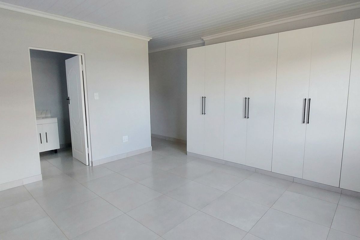 A bright, spacious bedroom featuring neutral floor tiles, built-in white cabinetry, and direct access to an en-suite bathroom.