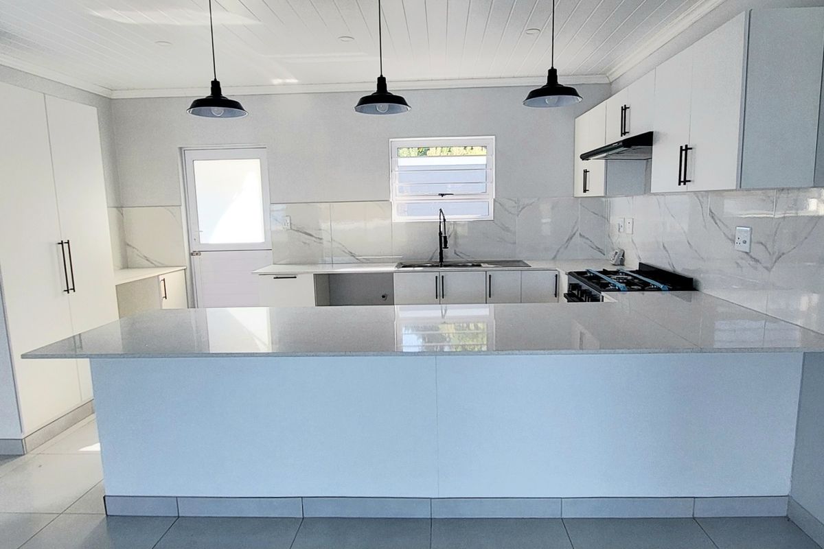 Modern kitchen featuring white cabinetry, stone countertops, marble-look splashback, integrated gas hob, and a breakfast bar island with pendant lighting.