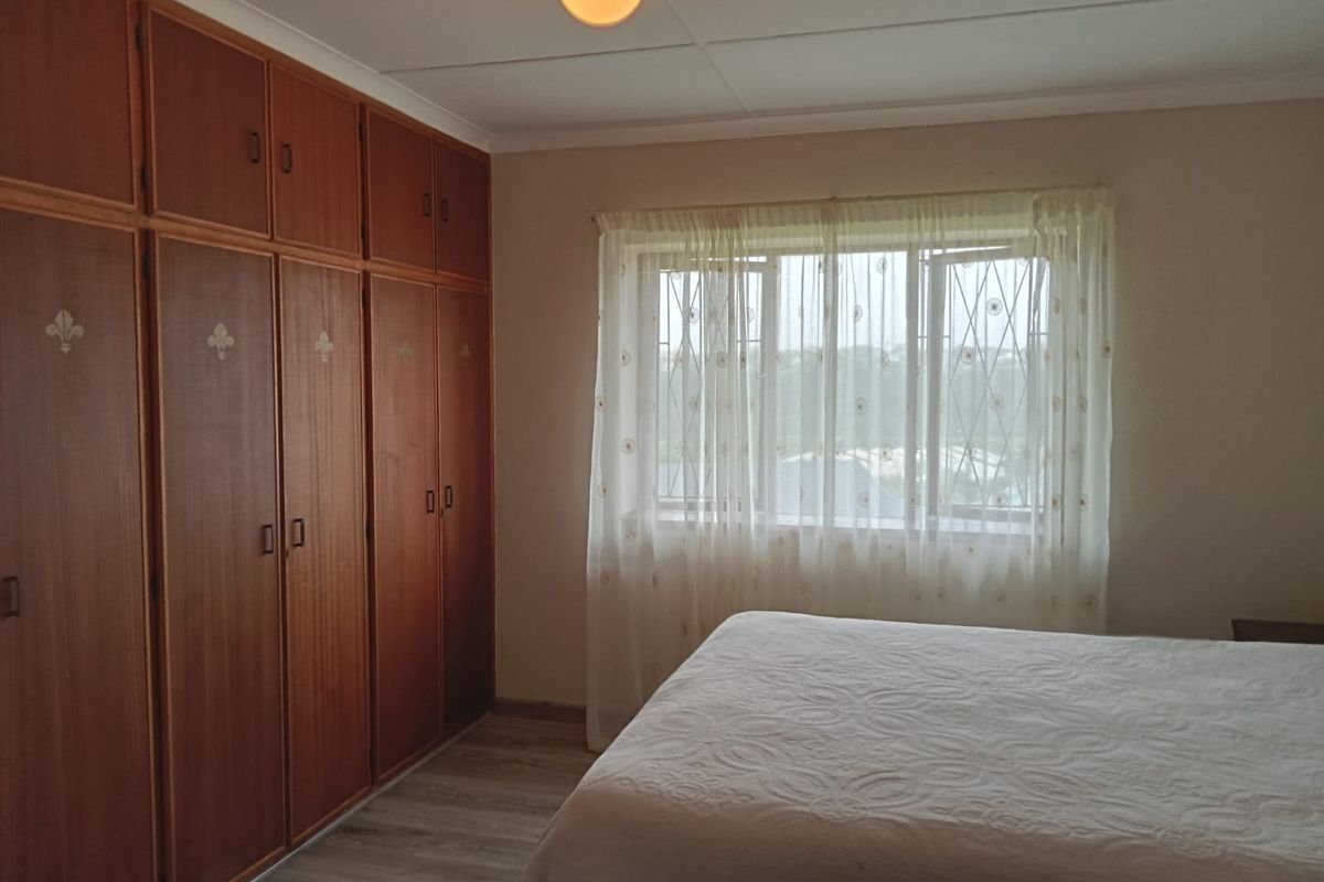 A bedroom featuring extensive built-in wooden cabinetry, laminate flooring, and a window fitted with security bars.
