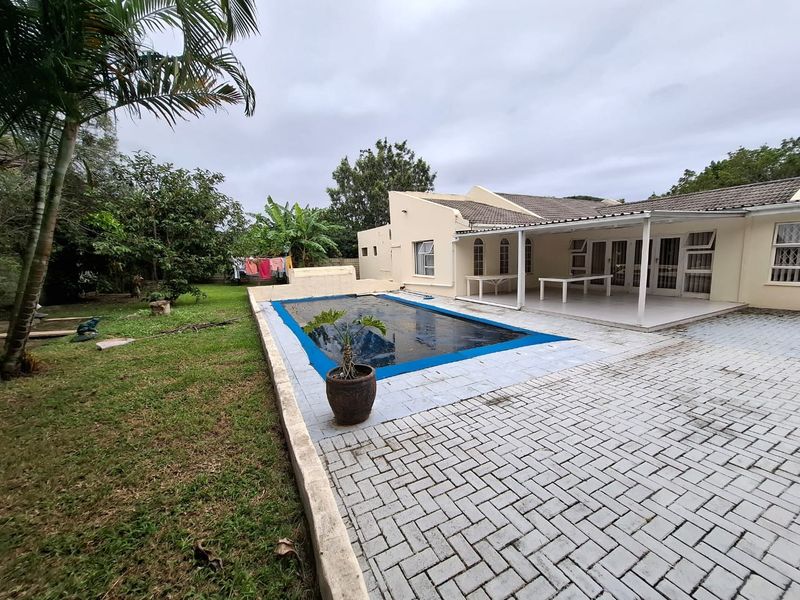 Rear exterior view featuring a swimming pool with cover, paved patio area, and a spacious garden.