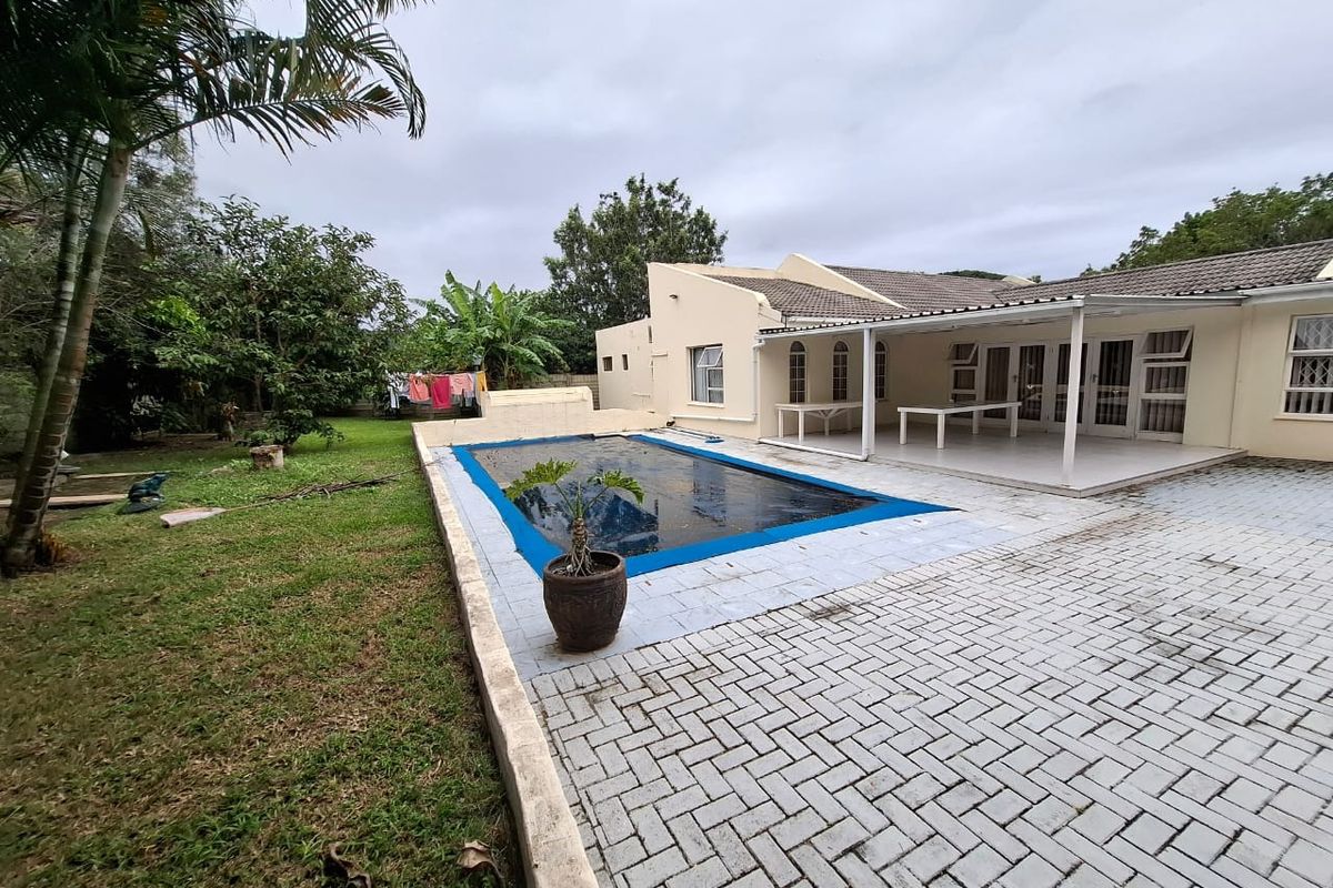 Rear exterior view featuring a swimming pool with cover, paved patio area, and a spacious garden.