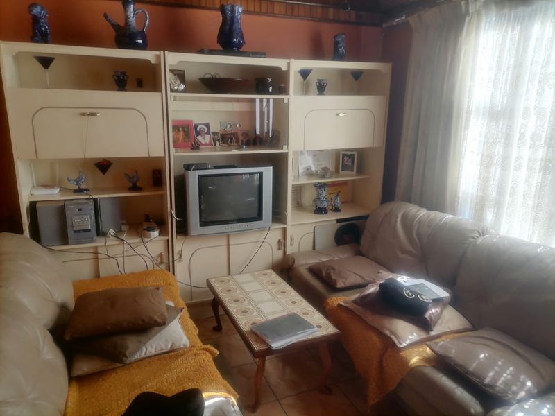 A living room featuring a large built-in wall unit and tiled flooring, currently furnished with seating and a coffee table.