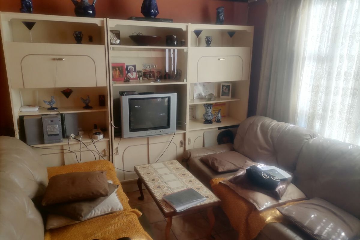 A living room featuring a large built-in wall unit and tiled flooring, currently furnished with seating and a coffee table.