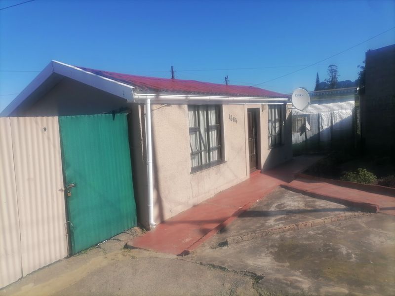 Front view of a single-story residential house featuring a red corrugated metal roof, concrete walkway, and perimeter metal fencing.
