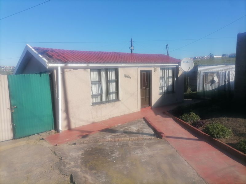 Front view of a single-story house featuring a corrugated metal roof, plastered walls, and a concrete driveway with a painted walkway.