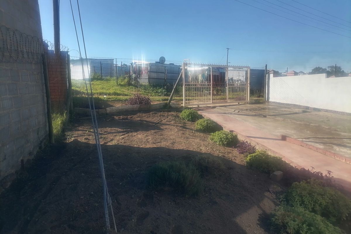 Rear yard area featuring a metal sliding gate, perimeter fencing with razor wire, and a concrete driveway section.