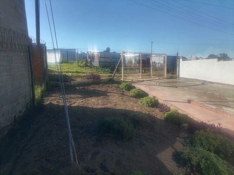 Rear yard area featuring a metal sliding gate, perimeter fencing with razor wire, and a concrete driveway section.