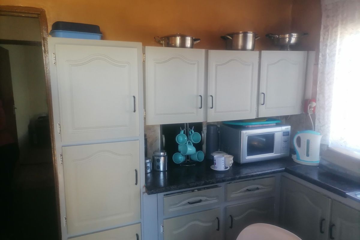 A compact kitchen featuring built-in cabinetry, laminate countertops, and a built-in microwave, offering a functional layout in need of cosmetic updates.