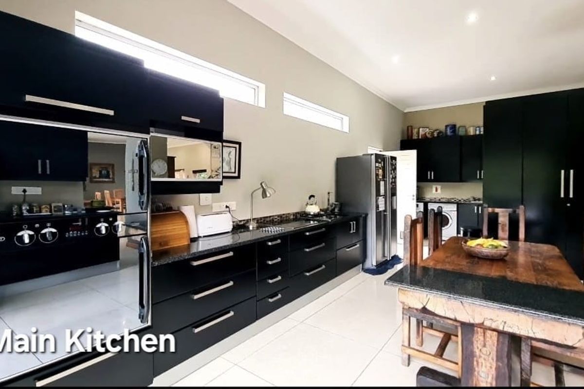 Spacious kitchen featuring modern black cabinetry, granite countertops, built-in oven, and hob, with tiled flooring and recessed lighting throughout.