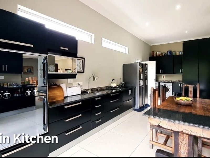 Spacious kitchen featuring modern black cabinetry, granite countertops, built-in oven, and hob, with tiled flooring and recessed lighting throughout.