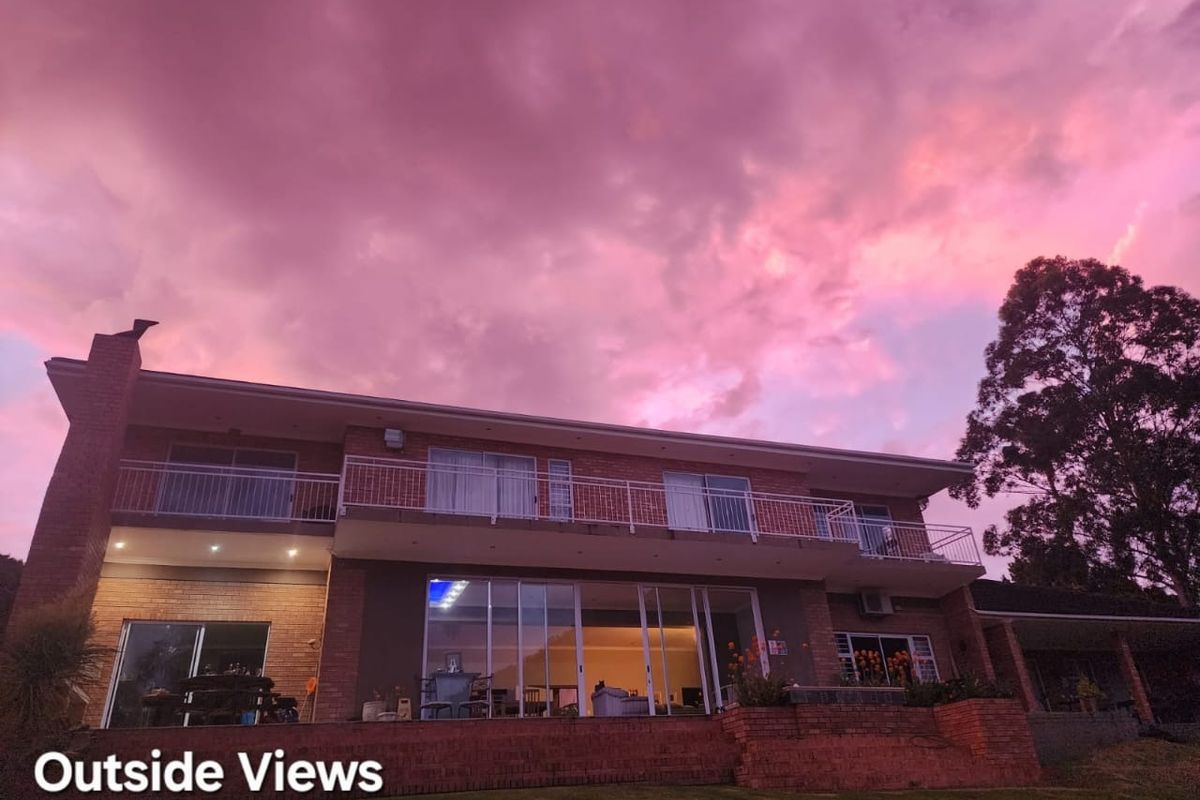 Rear exterior view of a two-story brick guest house featuring a balcony, large sliding glass doors, and a sunset sky.
