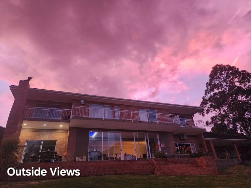 Rear exterior view of a two-story brick guest house featuring a balcony, large sliding glass doors, and a sunset sky.