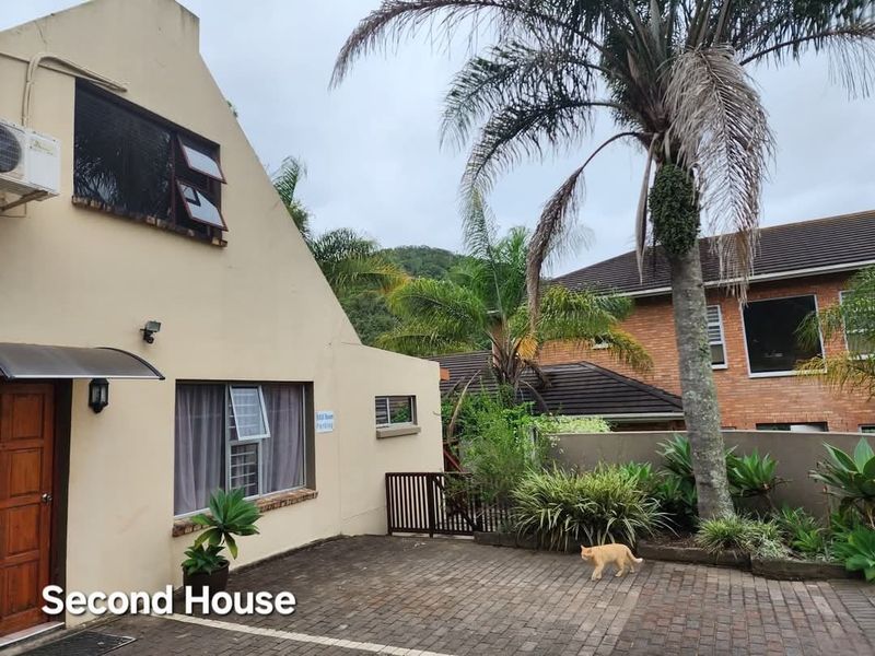 Exterior view of the guest house featuring a paved driveway, entrance area with awning, and established garden surroundings.