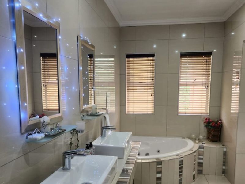 A well-appointed bathroom featuring a double vanity with modern basins, tiled finishes, and a built-in corner bathtub with integrated lighting.