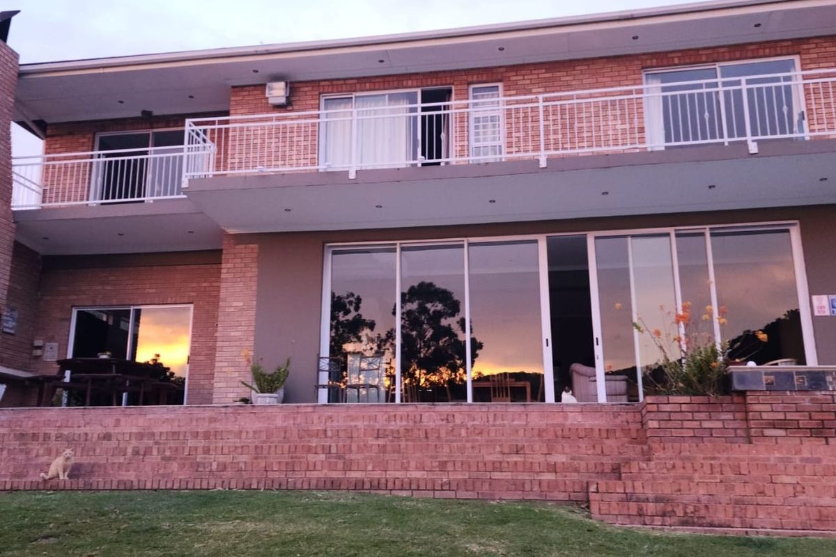 Rear view of a two-story brick guest house featuring a spacious patio, large sliding glass doors, and an upper-level balcony with metal railings.