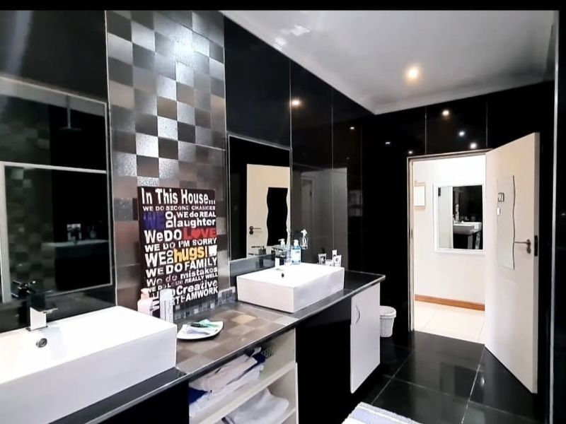 Modern bathroom featuring a double vanity with vessel sinks, high-gloss black wall tiles, and contemporary finishes.
